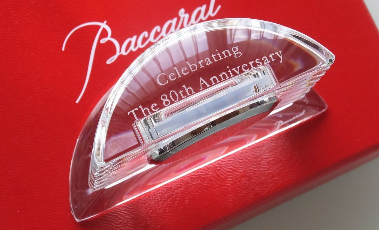 バカラの『ラランド クロック』の上部クリスタル部分に、『80周年記念』の文字を格調高く名入れ彫刻した写真。天体観測者ラランドの名を冠した円形の美しい造形に、80年の歴史を祝う精緻な刻印が施されており、クリスタルの純粋な透明感と正確な時を刻む時計が、企業の長きにわたる功績と繁栄を象徴する最高級の周年記念ギフトのイメージ。