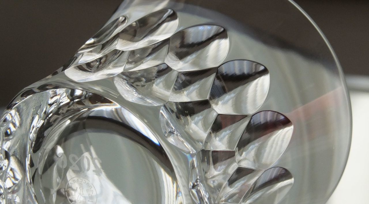 バカラのイヤーグラス、ダリア（Dahlia）タンブラー2026が横に倒して置かれ、その側面全体を捉えたクリスタルカットのクローズアップ写真。ダリアの花弁をモチーフとしたダイナミックかつ複雑なV字カットが、光を多角的に集めて反射させ、万華鏡のような輝きを生み出している様子が鮮明に写っている。世界最高峰のクリスタル職人による緻密な手仕事と、グラスの持つ芸術的な造形美を強調したディテール。