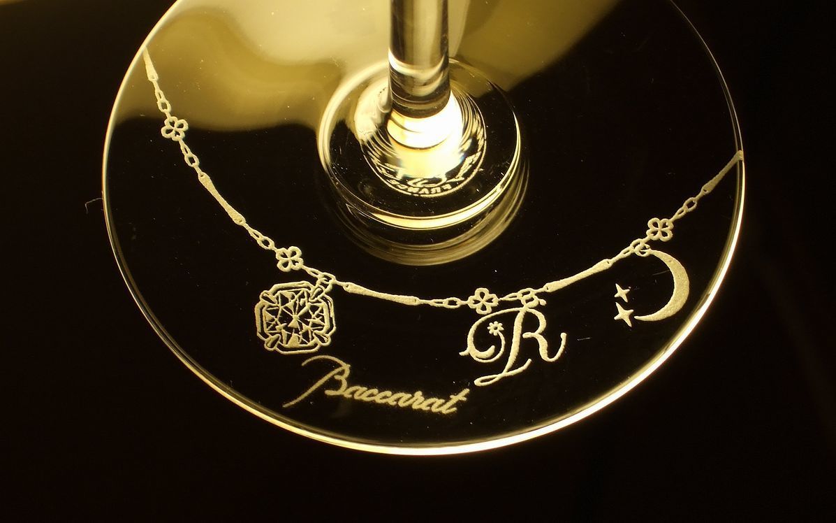 バカラ（Baccarat）の『アリア』タンブラーの底面に、記念日とお名前が精緻に名入れ彫刻された写真。洗練された流線型のカットが施された最高級クリスタルガラス越しに、底面の記念刻印が美しく浮かび上がり納車記念日の大切な節目を祝福する特別感あふれるパーソナライズドギフトにふさわしいイメージ。