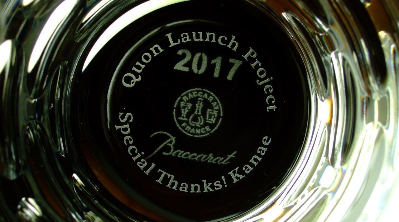 バカラ（Baccarat）のクリスタルタンブラーの底面に、英語で『Quon Launch Project Special Thanks Kanae』と精緻に名入れ彫刻された写真。最高級クリスタルならではの透き通る輝きに、プロジェクトの立ち上げ成功を祝し貢献したメンバーへ感謝を伝える刻印が美しく施され、ビジネスプロジェクトの完了記念やチームメンバーへの特別な贈答ギフトにふさわしい格調高いイメージ。