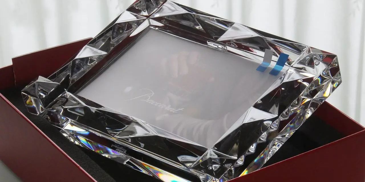バカラの『ルクソール』フォトフレームが、ブランドの象徴である鮮やかなレッドボックスに収められた写真。世界遺産エジプトのルクソールから名付けられた、ピラミッド状のダイヤモンドカッティングが放つ幾何学的な輝きと、赤いギフトボックスの高級感が重なり合い、大切な思い出を飾るにふさわしい格調高い贈答品のイメージ。