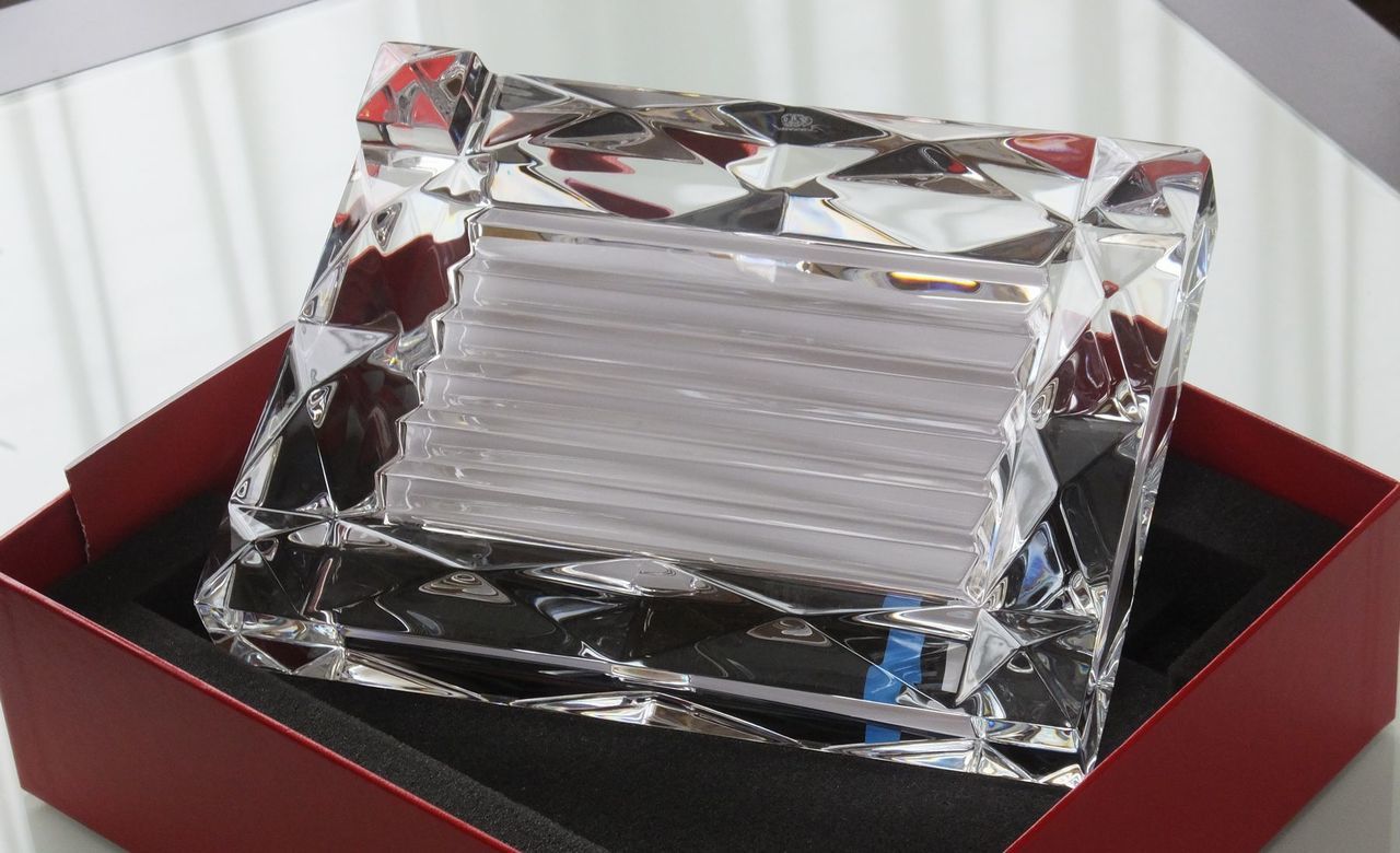バカラの『ルクソール』フォトフレームを横置きにし、写真を入れていない状態でテーブルに置いた写真。ピラミッド型のダイヤモンドカッティングが施された厚みのあるクリスタルの塊が、周囲の光を複雑に透過・屈折させ、まるで純粋な彫刻作品のような圧倒的な透明度と輝きを放つ、名入れ彫刻前の美しさを際立たせたイメージ