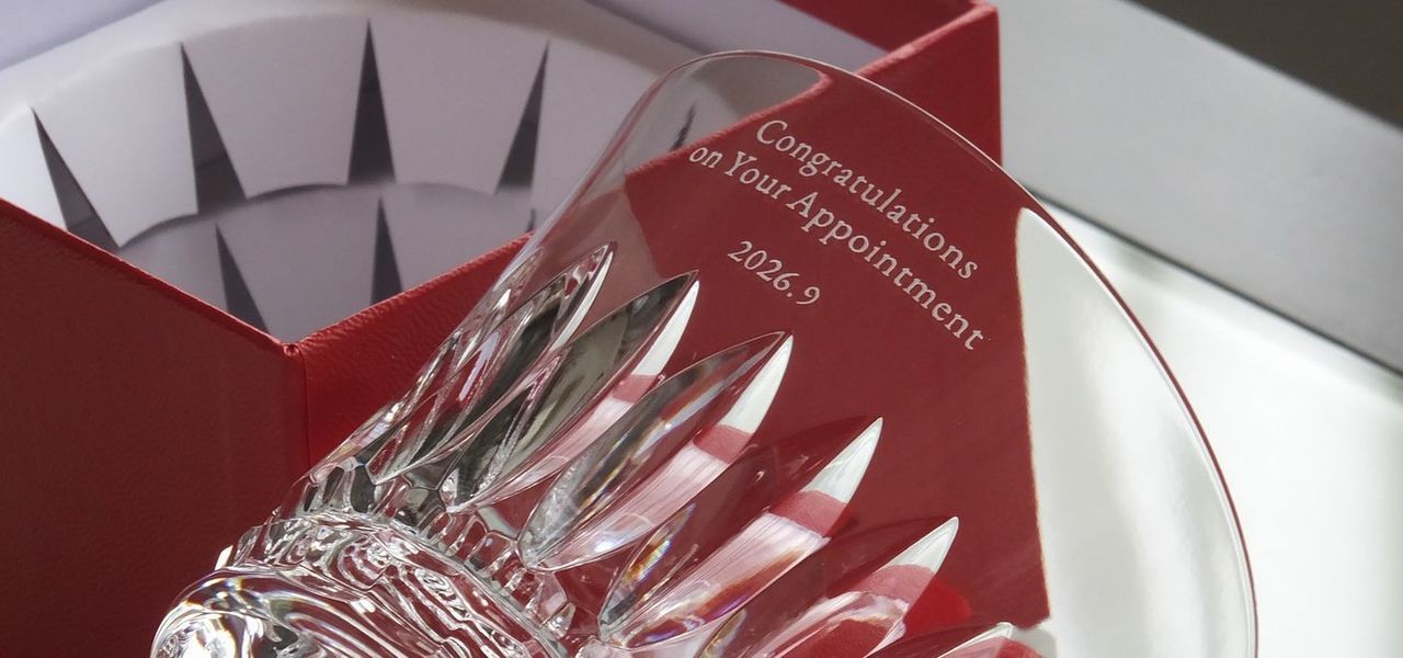 バカラ（Baccarat）の2026年年号刻印入りイヤーグラス『ダリア タンブラー』の側面に、『Congratulations on your appointment 2026.9』の昇進・就任祝いメッセージが精緻に名入れ彫刻され、ブランドを象徴する深紅のボックス（レッドボックス）の上に設置された写真。大輪のダリアをイメージした可憐でラグジュアリーなカットワークと最高級クリスタルガラスの透明感が、ブランドカラーの赤い箱の上でいっそう美しく際立ち、ビジネスでの新たな躍進や栄誉ある役員・社長就任を祝福する最高峰のメモリアルギフトイメージ。