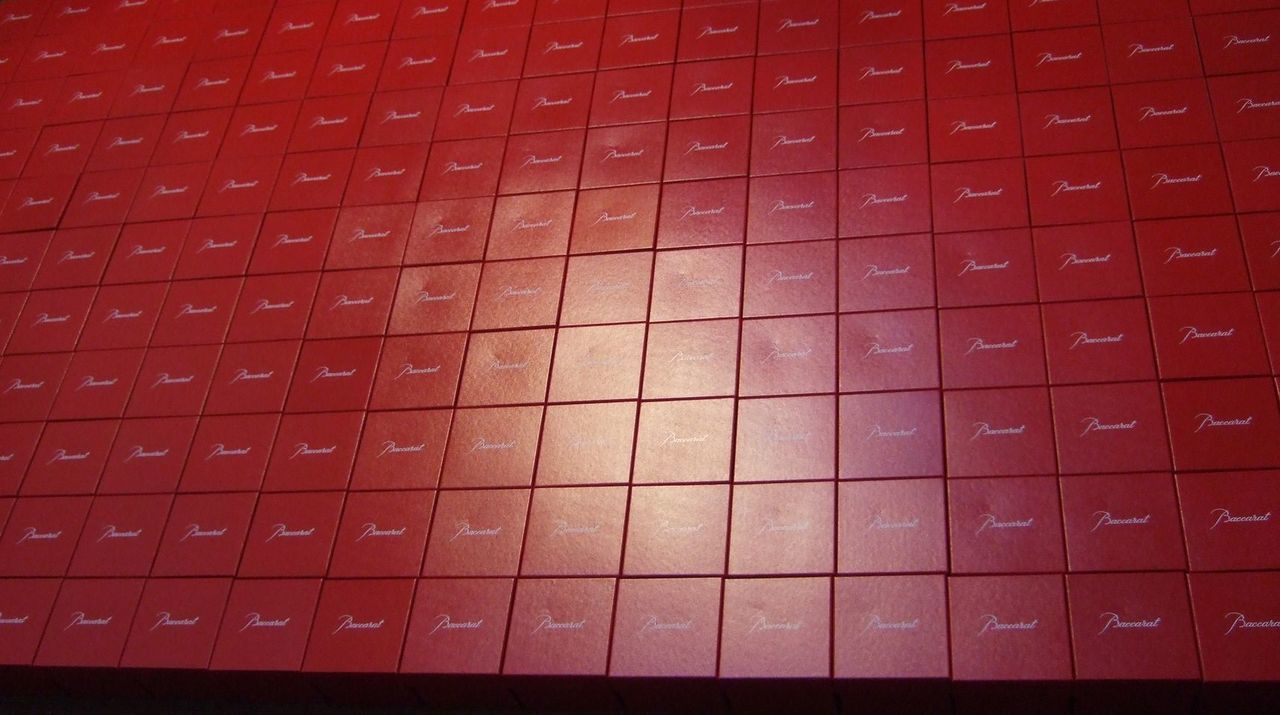 企業の株式上場を記念した贈呈品として、200個を超えるバカラのレッドボックスが会場や倉庫に整然と積み上げられ、画面いっぱいに広がっている圧巻の写真。バカラの象徴である鮮やかな赤い箱が、整然と並ぶことで生まれる幾何学的な美しさと、上場という一大イベントの規模の大きさを物語っている。箱の中には、上場記念の名入れ彫刻を施した2019年イヤーグラス『ヴィータ』が収められており、ステークホルダーへの感謝の総量と、企業の新たな門出を祝う華やかさが最高潮に達している様子を視覚的に表現している。