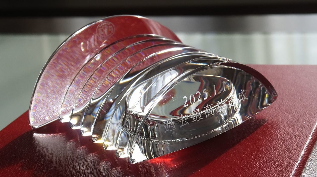 バカラのクリスタル製置き時計『ラランドクロック』の上部に、企業の過去最高益達成を祝した名入れ彫刻を施したサンプル画像。円形クリスタルの上部アールに沿って、『2025.1.14 過去最高益達成！』の文字が、躍動感と力強さを感じさせる端正な書体で精緻に刻印されている。バカラ特有の最高級の透明度と、時計を包み込む重厚なクリスタルの輝きが、社員一丸となって成し遂げた歴史的な快挙と、さらなる飛躍を目指す新しい時を象徴しており、企業の金字塔を永遠に称え続けるための、誇り高く品格に満ちた特別なアニバーサリーギフトであることを視覚的に表現している。