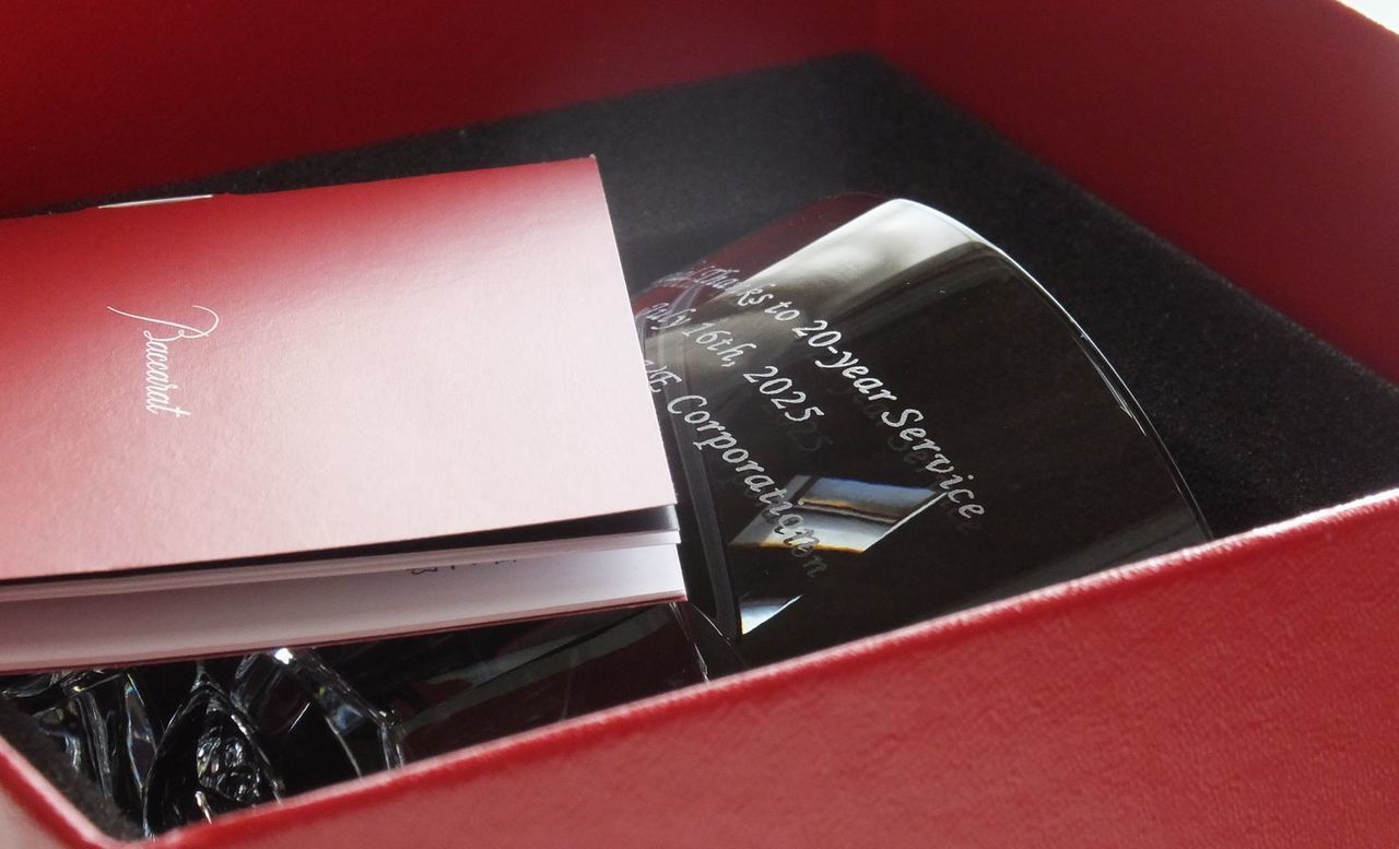 バカラの『アビス（深淵）』タンブラーの側面に、永年勤続を称える記念メッセージを精緻に名入れ彫刻した写真。六角形の重厚な底部から続くフラットな面に、長年の功労への感謝を込めた言葉がクリスタルの輝きとともに美しく刻まれており、多面的なカッティングが放つ独特の光の反射が、表彰にふさわしい荘厳な品格を醸し出す最高級ギフトのイメージ。
