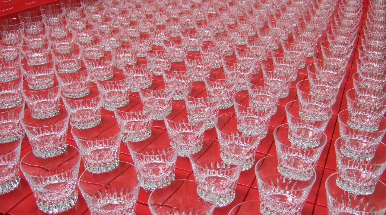 バカラ（Baccarat）を象徴する鮮やかなレッドボックス（赤箱）の上に、100個以上のバカラ製クリスタルタンブラーが圧巻のスケールで整然と並べられた写真。最高級ブランドならではの気品ある輝きと圧倒的な存在感を放ち、企業の100周年記念や大型式典、特別な記念事業における大ロット名入れギフト・記念品納品実績の確かさと格調高さを象徴するイメージ。