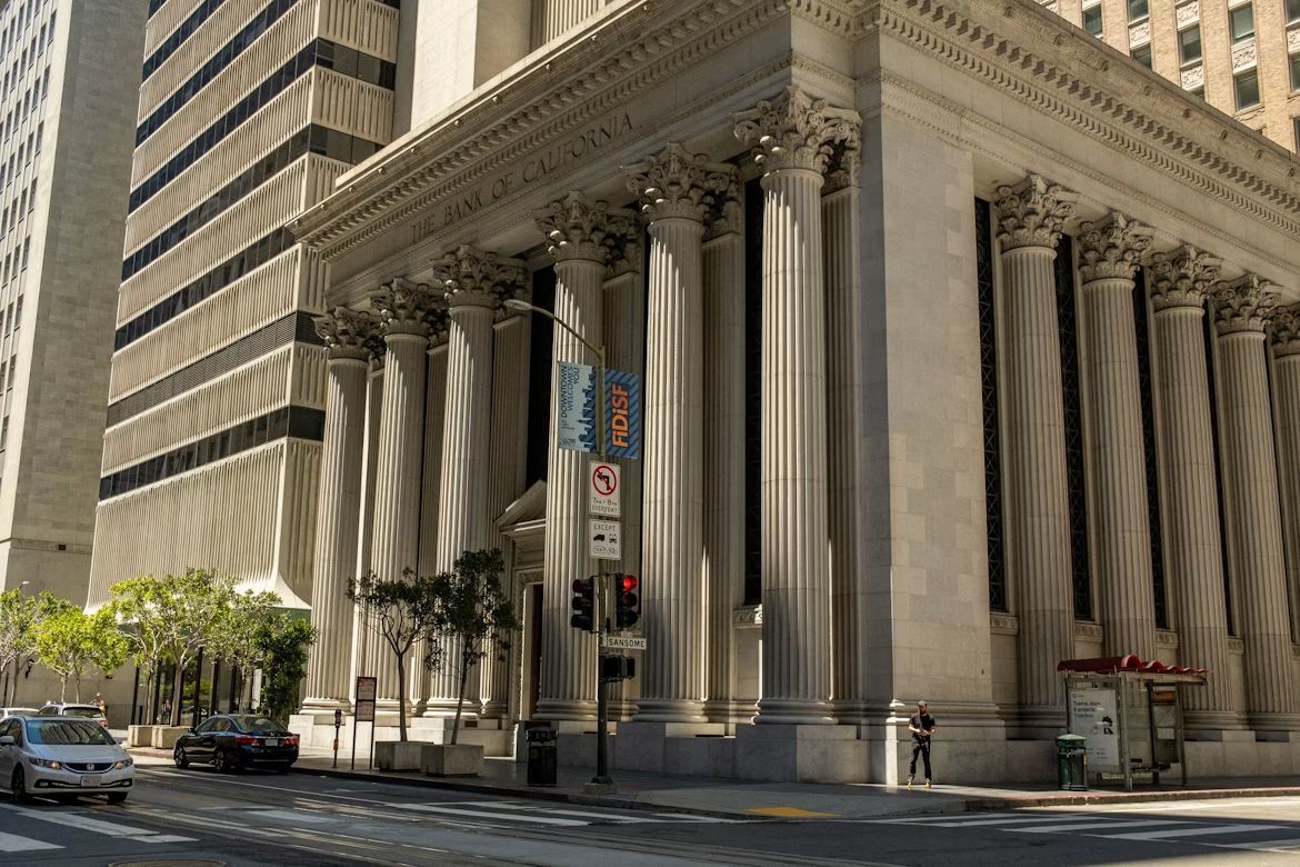 ザ・バンク・オブ・カリフォルニア（The Bank of California）の重厚な歴史的建造物の外観を捉えた写真。クラシックなギリシャ復活様式やコリンス式の巨大な石柱、格式高いファサードが立ち並び、金融機関としての長い伝統と信頼感、歴史的建築物ならではの荘厳で格調高い構えを象徴するイメージ。