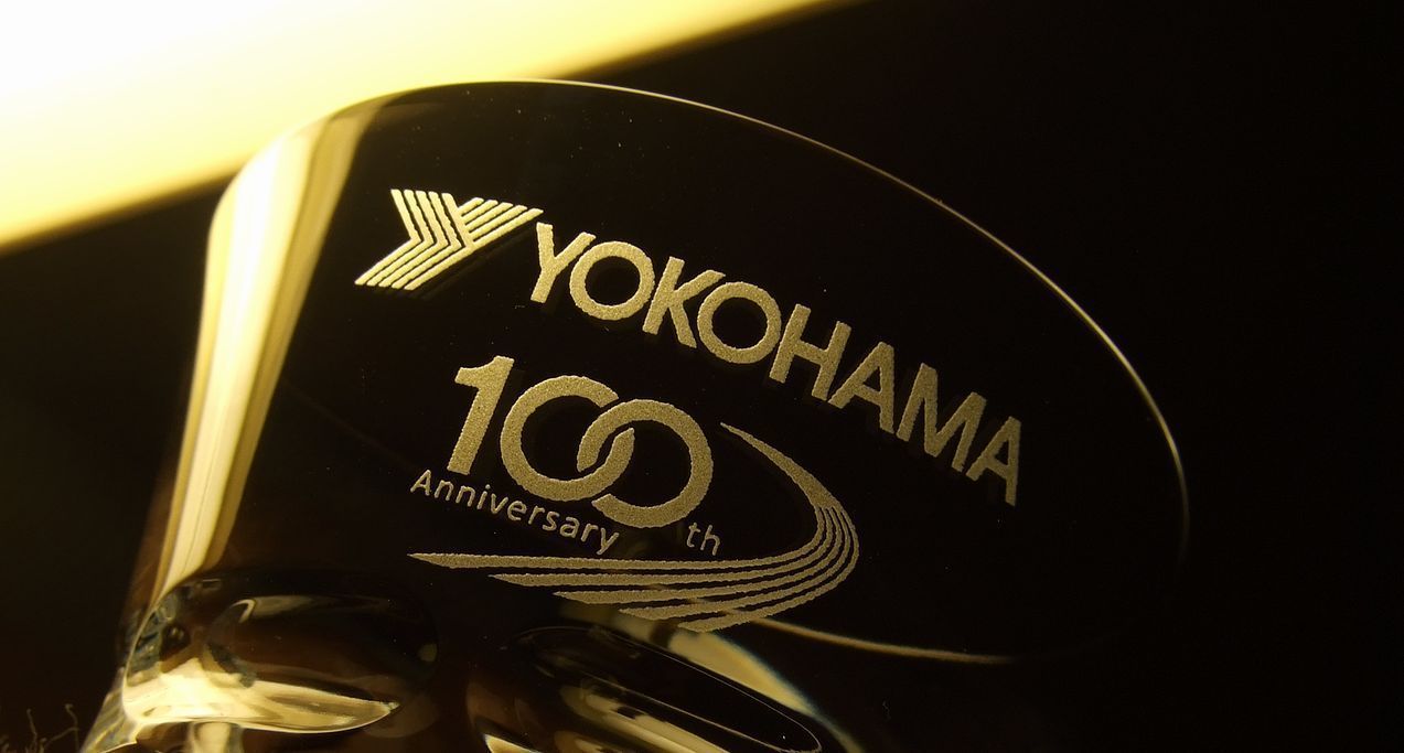 バカラ（Baccarat）のクリスタルタンブラーの側面に、『横浜ゴム（YOKOHAMA）創業100周年記念』のロゴデザインが精緻に名入れ彫刻された写真。最高級クリスタルならではの透明感と輝きに、100年の歴史を称える記念ロゴが美しく刻み込まれ、企業の偉大な節目と功績を祝う最高峰の記念品・法人ギフトにふさわしい格調高いイメージ。