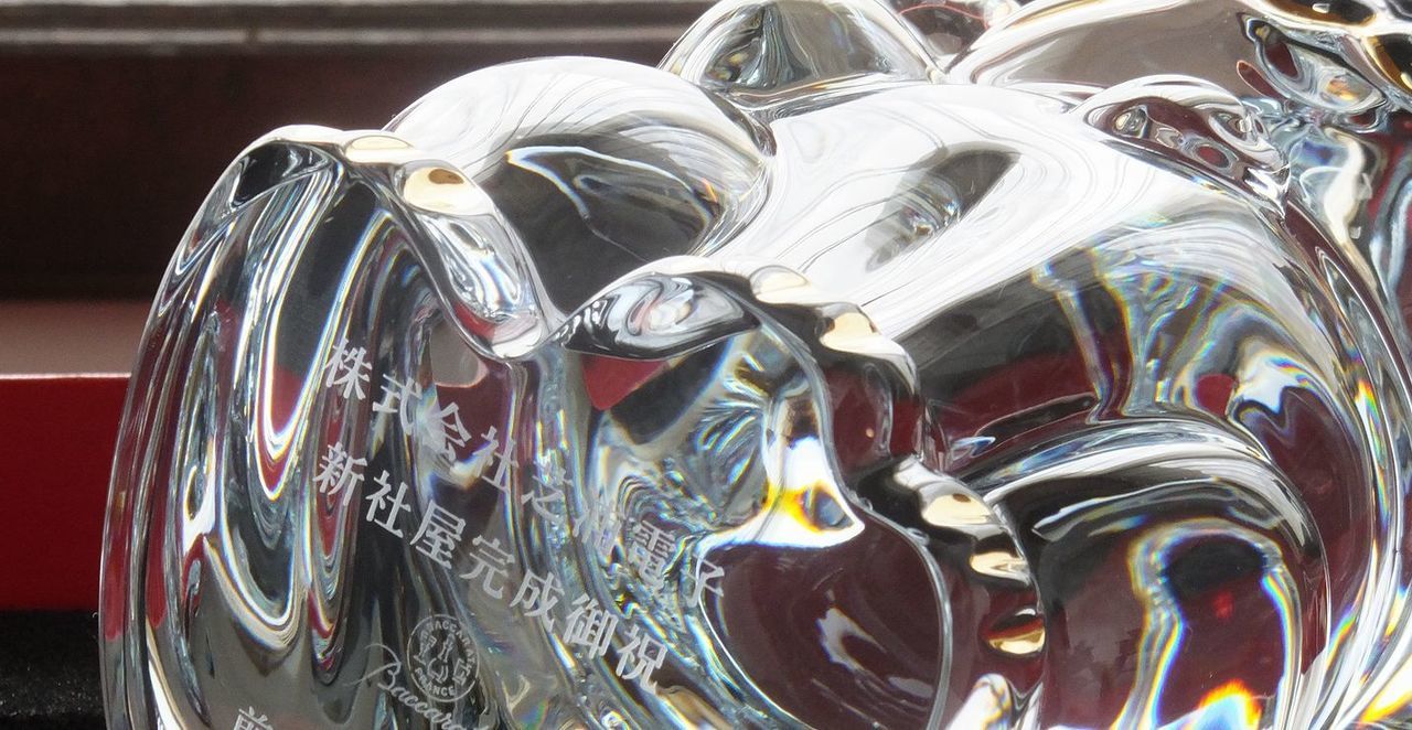 バカラ 招き猫XLに新社屋完成祝いのメッセージが名入れ彫刻されている透明で輝くクリスタル製の縁起物。竣工祝いに最適な、目標達成や社業繁栄を願う特別な贈り物。