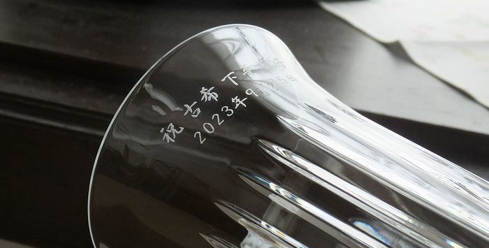 バカラ（Baccarat）のクリスタル花瓶『ビゾー ベース』の側面に、漢字で『祝 古希』、お名前、および日付が精緻に名入れ彫刻された写真。鋭い斜めのカットが光を複雑に反射する最高級クリスタルならではの重厚な輝きに、70歳の長寿と人生の節目を祝福する刻印が映え、古希祝いや敬老の日の贈り物、特別なお祝いにふさわしい最高峰の格調高いギフトのイメージ。