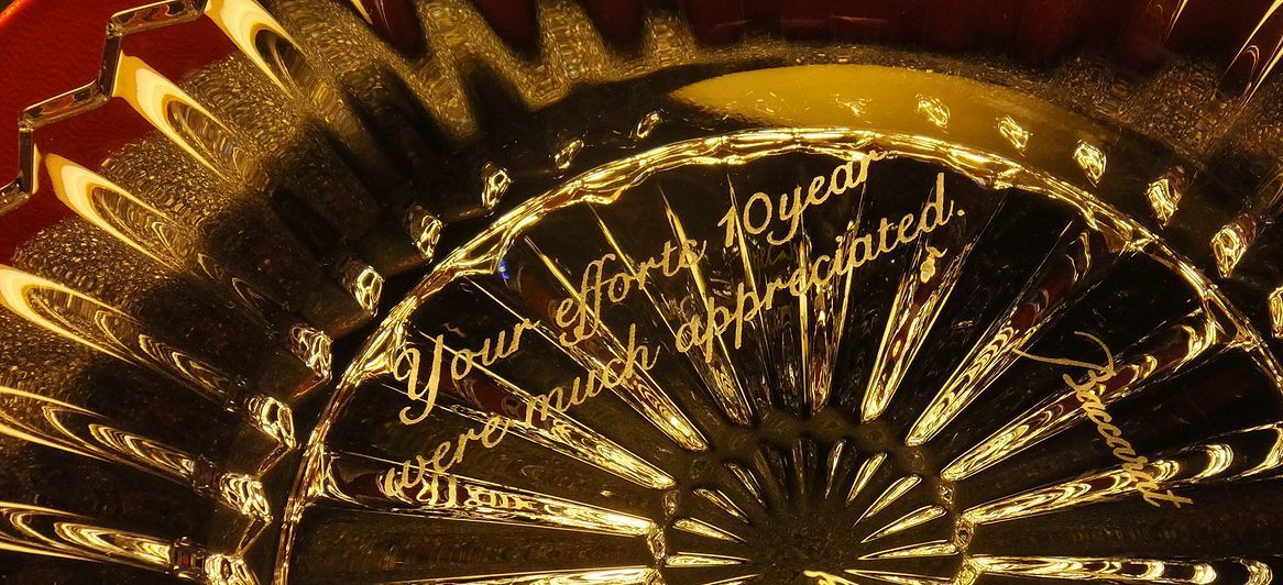 バカラのミルニュイ（Mille Nuits）プレート（皿）のクリスタル部分に、『Your efforts 10 year were much appreciated』（あなたの10年間の努力に心から感謝します）という10周年を記念する感謝のメッセージが名入れ彫刻されたクローズアップ写真。ミルニュイ特有のプリーツ状の緻密なカットの中に、長きにわたる貢献への敬意と深い感謝の気持ちが深く鮮明に刻まれている。世界最高峰の輝きが、功労者の栄誉を末永く称える格式高い記念品としての存在感。