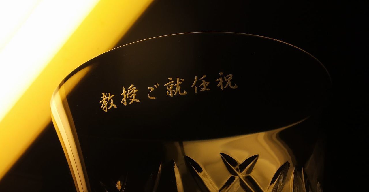 バカラ（Baccarat）の年号入りイヤー タンブラー『アリア（2025年）』の側面に、漢字で『教授ご就任祝』の文字が精緻に名入れ彫刻された写真。最高級クリスタルならではの透き通る輝きと優美なカットに、学術・研究分野における最高の栄誉と長年の功績をたたえる刻印が美しく施され、教授就任のお祝いや恩師・研究者へ贈る最高峰の特別なお祝いギフト・記念品にふさわしい格調高いイメージ。