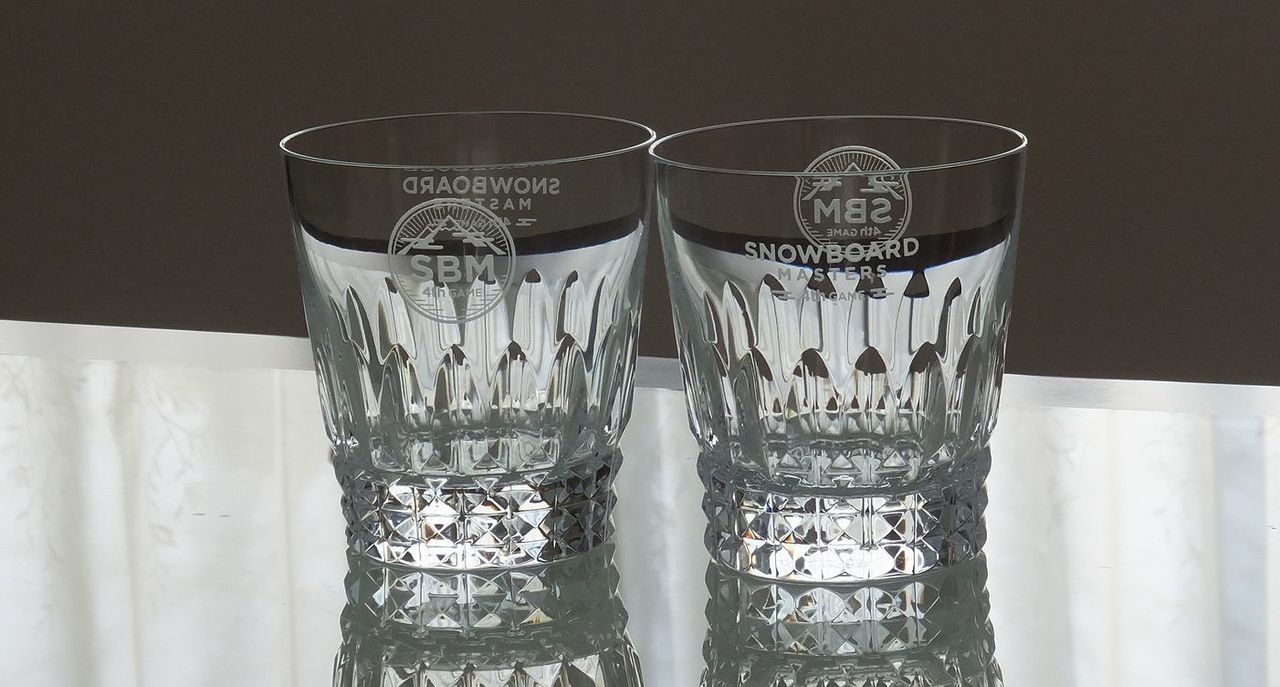 バカラ（Baccarat）の『ピカデリー タンブラー』2個セットの側面に、それぞれ『第4回スノーボードマスターズ』の大会ロゴと大会タイトルが精緻に名入れ彫刻されたペアグラスの写真。ロンドンのピカデリー広場から名付けられた伝統的な格子状の幾何学カットが美しい最高級クリスタルグラスに、スポーツの最高峰の栄誉と大会のメモリアルな記憶が映え、大会優勝・入賞トロフィーや特別記念品にふさわしい格調高いイメージ。