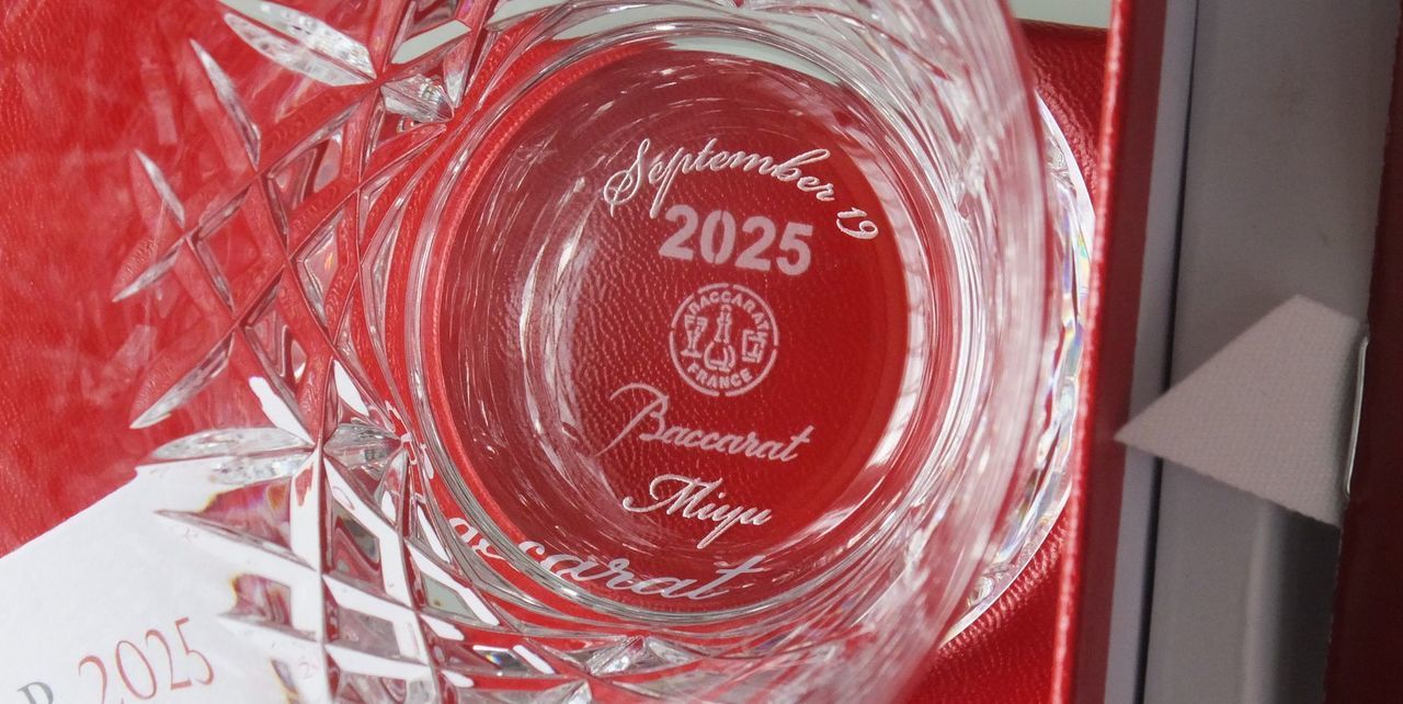 バカラ（Baccarat）の『アリア』タンブラーの底面に、記念日とお名前が精緻に名入れ彫刻された写真。洗練された流線型のカットが施された最高級クリスタルガラス越しに、底面の記念刻印が美しく浮かび上がり納車記念日の大切な節目を祝福する特別感あふれるパーソナライズドギフトにふさわしいイメージ。
