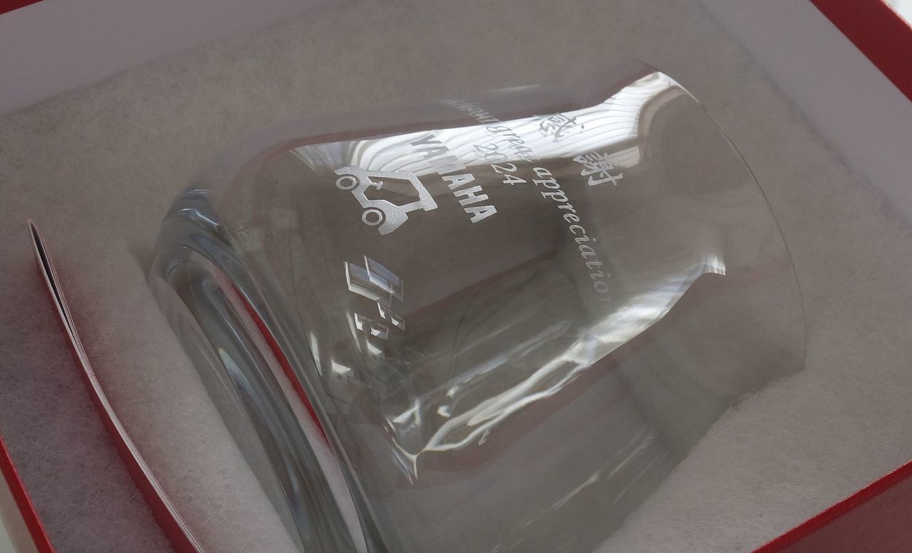 バカラの『シャトー タンブラー L』の側面に名入れ彫刻を施した退職祝い記念品の制作実績。ワインの香りを最大限に引き出すために設計されたシンプルなタンブラー側面に、『感謝 with great appreciation 2024』のメッセージとともに、YAMAHA（ヤマハ）のカート（またはそのロゴ・イラスト）をモチーフとしたオリジナルデザインが精巧に刻印されている。長年の功績と個人の趣味や携わった分野を融合させたこのデザインは、温かい労いと特別な心遣いを伝えるパーソナライズされた記念ギフトとして視覚的に伝えている。