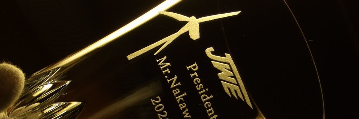 バカラ ヴィータ ハイボールグラスの側面に、社長就任祝いとして、企業名『JWE』のロゴ、風力発電のプロペラのイラスト、お名前、日付を名入れ彫刻した写真。『人生（VITA）』を象徴する多層的なカットと、クリーンエネルギー事業の未来を象徴するデザインが融合し、新しいリーダーの門出と企業の発展を力強く祝う、特別な記念品となっている。