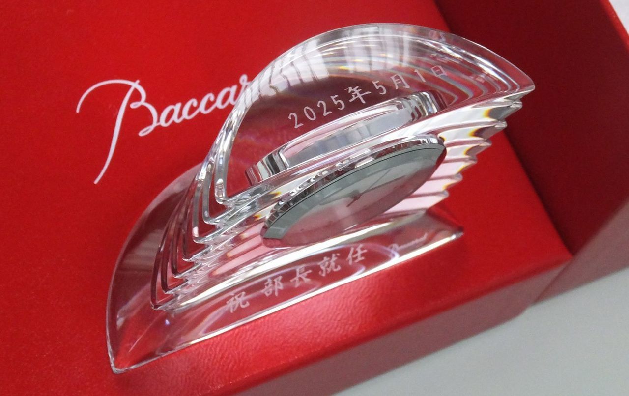 バカラ（Baccarat）の置き時計『ラランド クロック』の上部に記念日付、前面下部に『祝 部長就任』の文字が精緻に名入れ彫刻された昇進祝いの写真。重厚なクリスタルガラスの質感と眩い円形カットが美しく時を刻む最高級置時計に、躍進と更なる活躍をたたえる格調高い刻印が光を受けて映え、役員昇進や部長就任、社内昇格の栄誉を祝う法人・ビジネスシーンに最適な最高峰のメモリアルギフトイメージ。