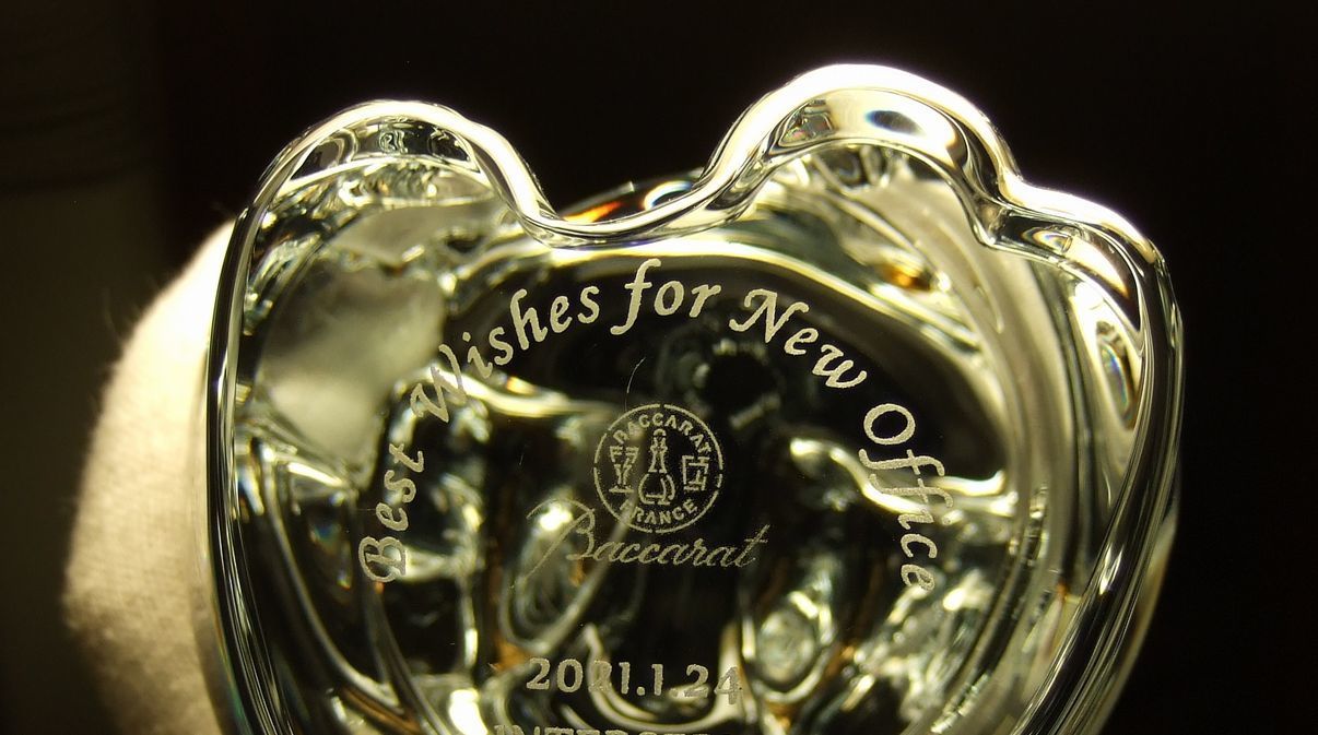 バカラのクリスタル製『招き猫 XLサイズ（高さ17cm）』の底面に、新オフィス開設祝いの彫刻を施したサンプル画像。安定感のある底面に、『Best Wishes for New office』のメッセージ、『日付』、そして『贈り主名』が、スタイリッシュで洗練された英字フォントで精緻に刻印されている。右手を挙げた存在感のある透明な招き猫が、新天地での千客万来と事業の隆盛を象徴しており、贈り主の温かい祝福と期待が込められた、新オフィスの受付や社長室を彩る最高級の縁起物であることを視覚的に表現している。