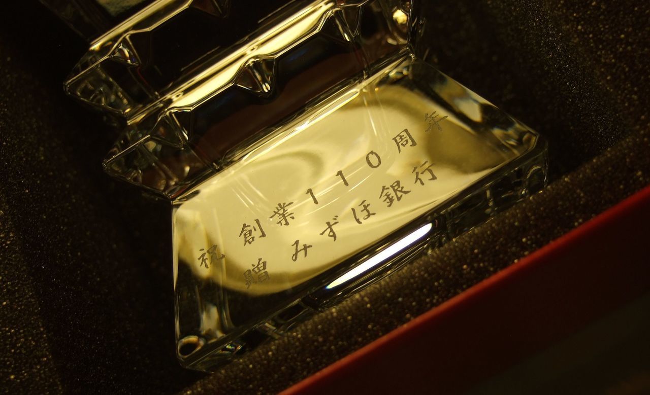 バカラ（Baccarat）のクリスタル製フラワーベース『コロンビーヌ』に、漢字で『祝 創業110周年 贈 みずほ銀行』と精緻に名入れ彫刻された写真。最高級クリスタルならではの幾何学的なカットと眩い輝きに、110周年の偉大な節目を祝う風格ある刻印が施され、企業の永続的な繁栄と発展を願う最高峰の周年記念ギフト・法人贈答品にふさわしい格調高いイメージ。