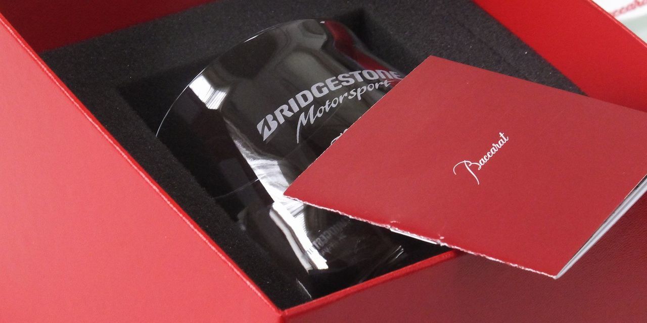 バカラ シャトーバカラ タンブラー Lサイズの側面に、退職祝いの記念として、所属していた部署やチームのロゴデザインを名入れ彫刻した写真。ブドウの房をモチーフとしたなめらかな曲線美を持つモダンなタンブラーに、チームへの貢献と絆を象徴するロゴが刻まれ、長年の労とチームからの感謝を形にした特別な記念品となっている。