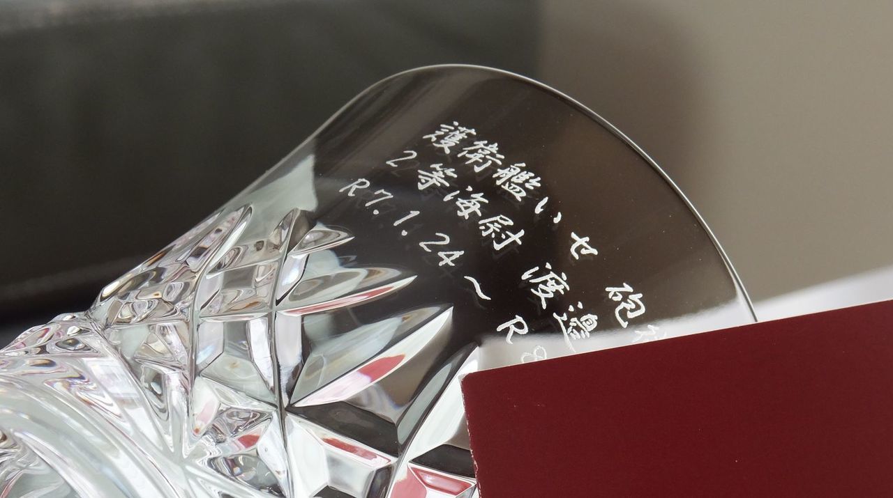バカラ（Baccarat）の年号入りイヤー タンブラー『アリア（2025年）』の側に、護衛艦『いせ』の艦名、階級（２等海尉）、個人名、および在籍期間が精緻に名入れ彫刻された写真。最高級クリスタルならではの優美な輝きと洗練されたカットに、洋上での任務と功績をたたえる誇り高い刻印が施され、自衛官の退官祝いや転任・記念品にふさわしい格調高いイメージ。