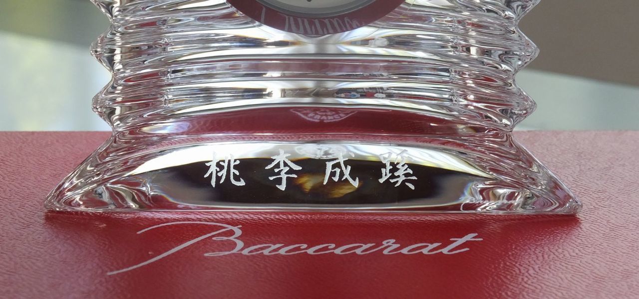 バカラ（Baccarat）の置き時計『ラランド クロック』の前面下部に、徳望のある人のもとには自然と人が集まることを意味する四字熟語『桃李成蹊』が精緻に名入れ彫刻された退職祝いの写真。重厚なクリスタルの立体感と眩い円形のカットが光を反射する最高級置時計に、長年の人徳と功績、恩師や上司への深い敬意を象徴する格調高い文字が美しく刻まれ、定年退職や役員退任、教授退官などの人生の節目の門出を祝う最高峰のメモリアルギフトイメージ。