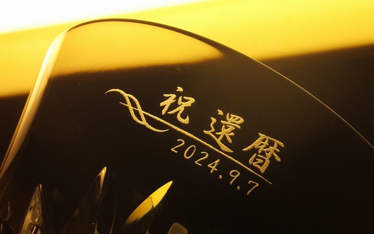 バカラ（Baccarat）の『ルテシア タンブラー 2024』の側面に、漢字で『祝 還暦』の文字、洗練された装飾バーデザイン、および日付が精緻に名入れ彫刻された写真。最高級クリスタルならではの透き通る輝きと年号刻印に、還暦（60歳）という人生の節目を華やかに祝福する彫刻が美しく映え、還暦祝いや長寿のお祝いに贈る最高峰のパーソナルギフトにふさわしい格調高いイメージ。
