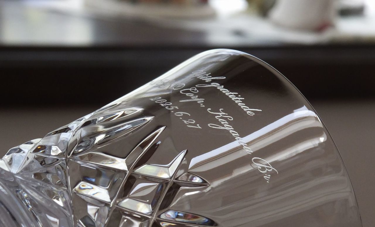 バカラの『アリア タンブラー』の側面に名入れ彫刻を施した退職祝い記念品の制作実績。空気が振動するさまをイメージしたデザインのタンブラーの側面に、メッセージ『with gratitude [企業名] [支店名] [日付]』が上品な英字フォントで精巧に刻印されている。モダンなクリスタルグラスに、感謝の意と長年の功績を証明する企業名・所属支店名、そして記念の日付を刻むことで、温かい労いと、組織を代表した深い敬意を伝える特別な記念ギフトとして視覚的に伝えている。