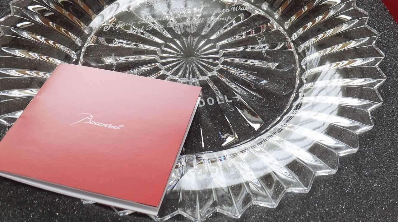 バカラ（Baccarat）のクリスタルプレート『ミルニュイ プレート』の上面に、グループ会社の代表へ向けた功績と貢献を称える英文メッセージが精緻に名入れ彫刻された写真。千の夜を意味する美しい放射状のカットと最高級クリスタルならではの輝きに、リーダーシップと長年の多大な功績をたたえる刻印が施され、グループ会社の周年記念、代表就任・退任の表彰、最高峰の法人贈答品にふさわしい格調高いイメージ。