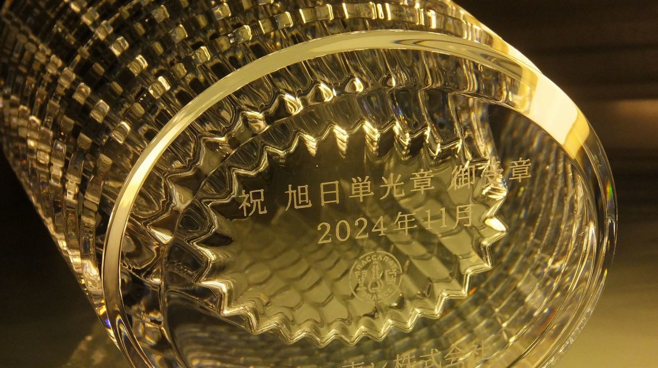 バカラ（Baccarat）のクリスタル花瓶『アイ ベース』の底面に、漢字で『祝 旭日単光章 御受章』の文字と受章年月日が精緻に名入れ彫刻された写真。最高級クリスタルならではの圧倒的な輝きと幾何学的なカットに、長年の社会的な功績と栄誉をたたえる格調高い刻印が美しく施され、叙勲・褒章のお祝いや記念品にふさわしい最高峰の贈答ギフトのイメージ。