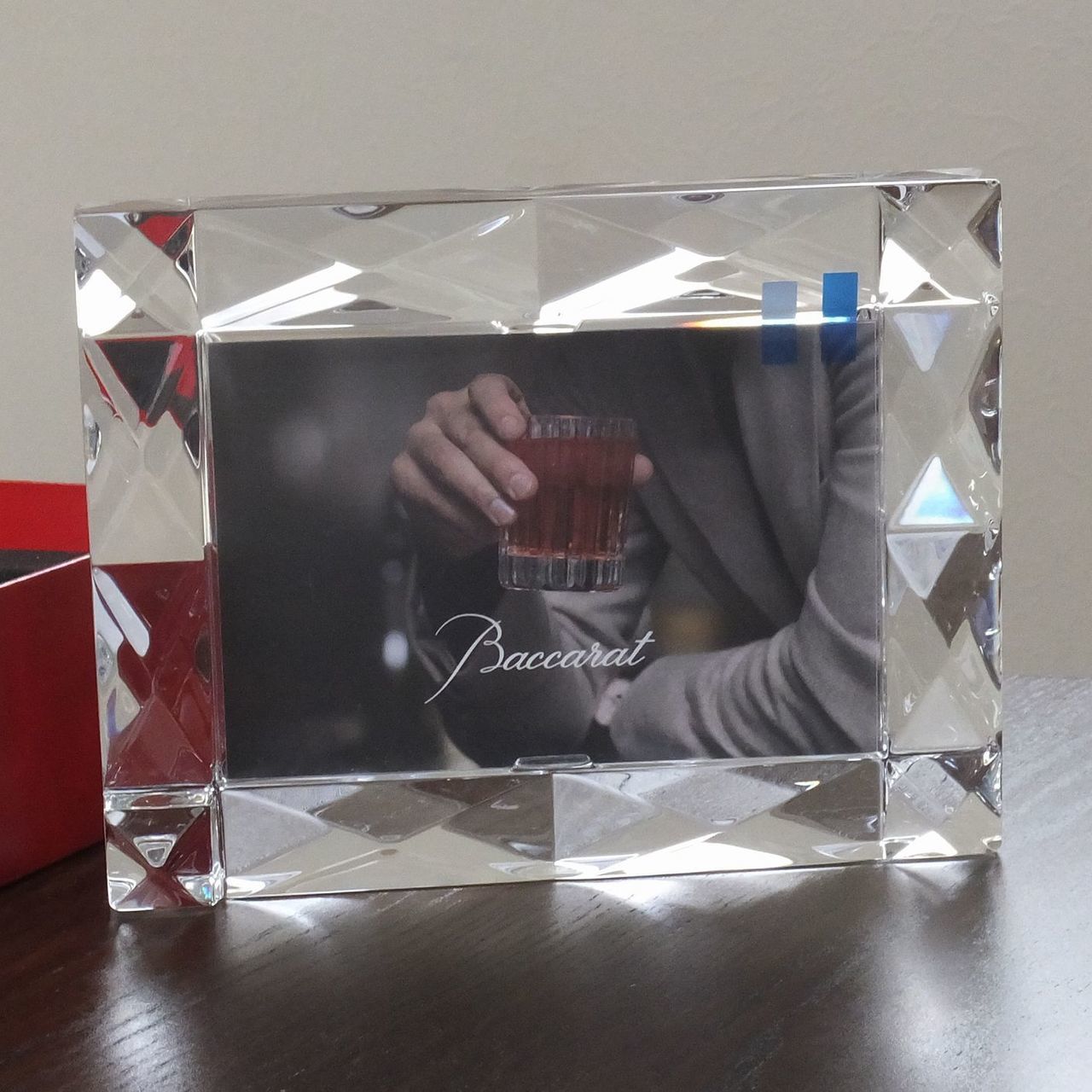 バカラの『ルクソール』フォトフレームを、テーブルの上に横置き（ランドスケープ）で配置した写真。エジプトのルクソールから着想を得たピラミッド型のダイヤモンドカッティングが光を複雑に反射し、モダンなインテリアの中で圧倒的な存在感とクリスタルの透明感を放つ、洗練された卓上フォトフレームのイメージ。