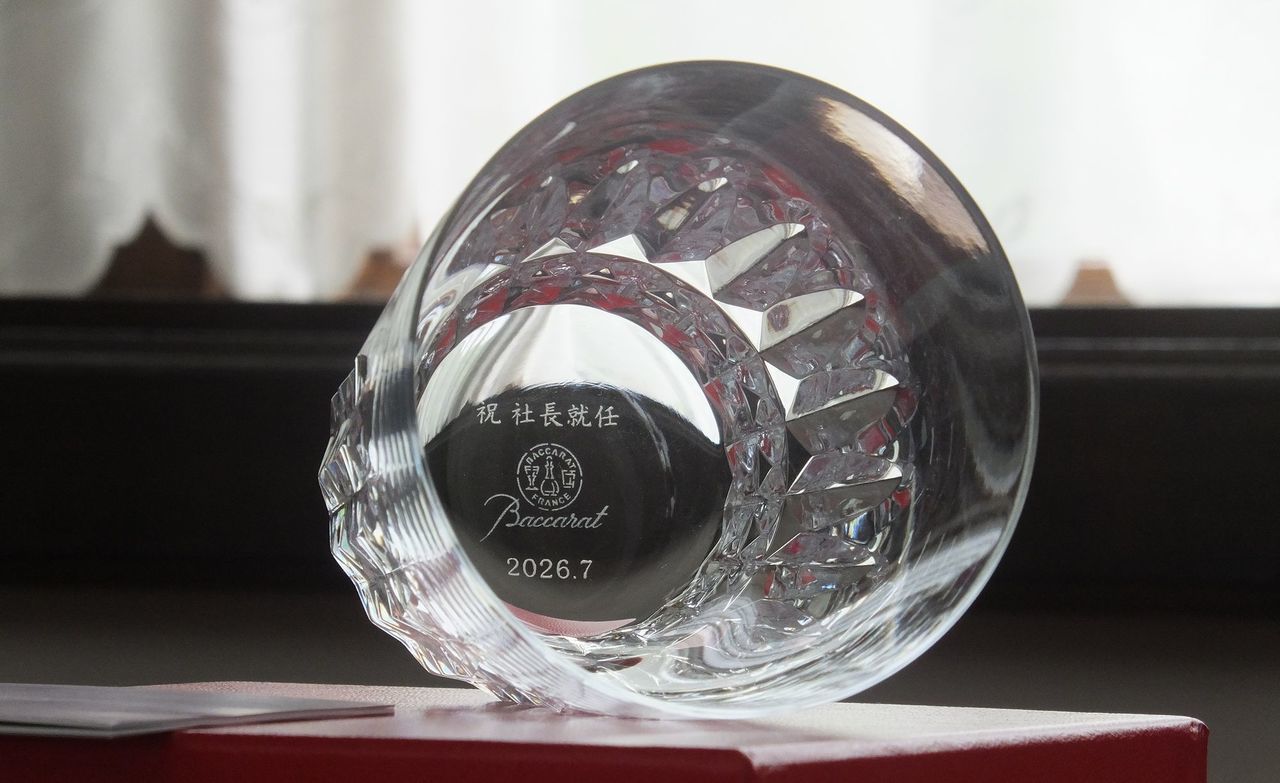 バカラ（Baccarat）の『ピカデリー タンブラー』の底面に、『祝 社長就任』の文字と『2026.7』の記念日付が精緻に名入れ彫刻された写真。伝統的なダイヤモンドカットの格子模様が華やかな光を放つ最高級クリスタルグラスの底から、新たなトップの就任と企業の繁栄を祝う刻印が密やかに美しく輝き、社長就任祝いや役員昇格、最高峰の法人お祝いギフトにふさわしい格調高いイメージ。