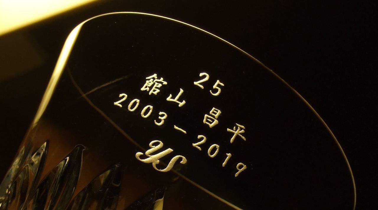 バカラの2019年限定イヤーグラス『ヴィータ』の底面に、ラグビーワールドカップ2019日本大会のベスト8進出を祝した名入れ彫刻を施したサンプル画像。グラスを覗き込んだ際に見える底面に、『RWC JAPAN BEST8』『ONE TEAM』の文字と『受贈者のお名前』が、力強く結束を感じさせる書体で精緻に刻印されている。グラス側面の複雑なカットが光を反射し、日本中が熱狂した歴史的快挙とチームの絆を象徴しており、一生に一度の感動を最高級のクリスタルに封じ込めた、誇り高き特別なアニバーサリーギフトであることを視覚的に表現している。