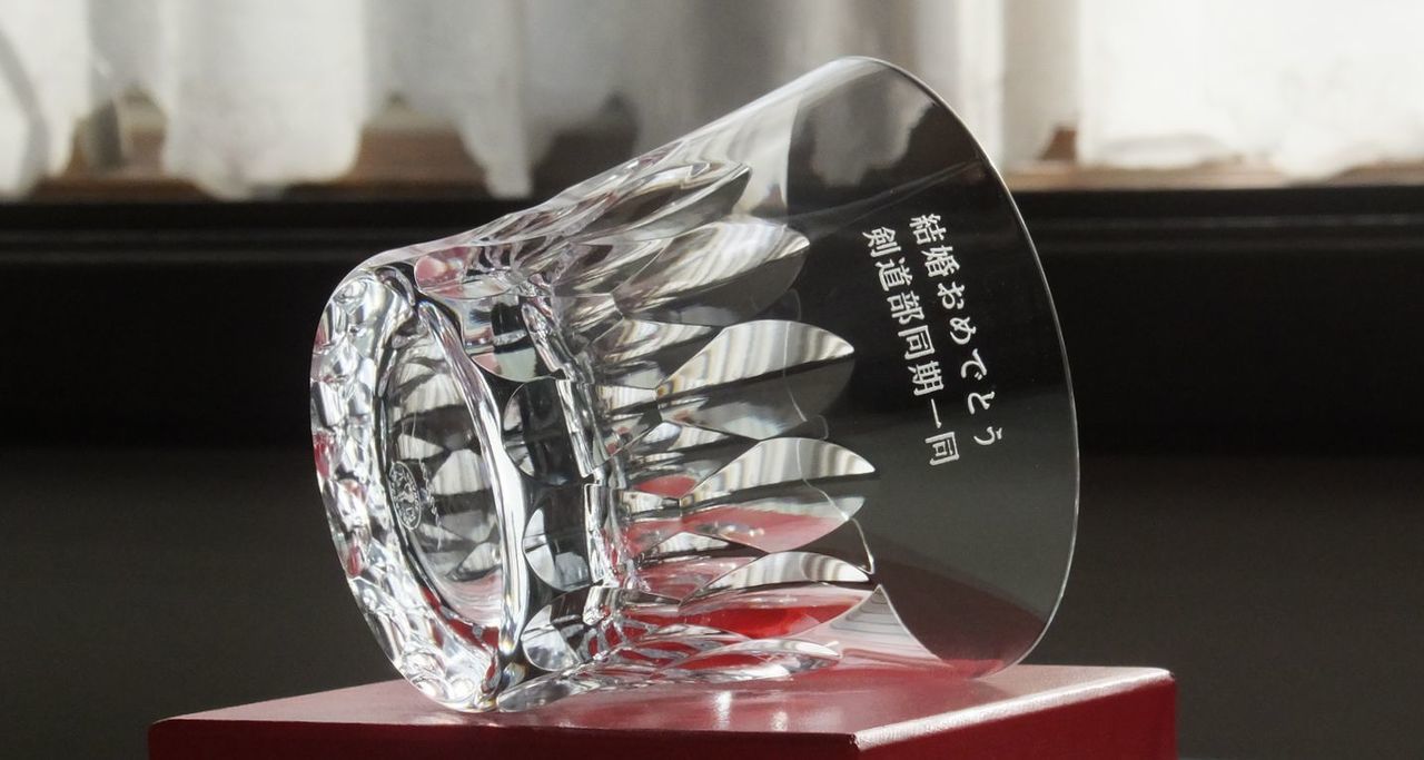 バカラのダリア タンブラー 2026の側面に『結婚おめでとう 剣道部同期一同』と名入れ彫刻を施した写真。クリスタルの輝きの中に仲間との絆を感じさせるメッセージが刻まれた、お祝いの場にふさわしい温かみと高級感を兼ね備えたパーソナライズギフトのイメージ。