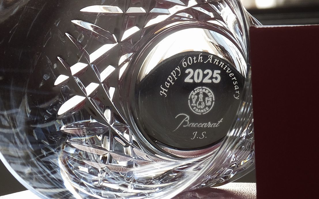 バカラのアリア(Aria)タンブラーのクリスタルグラスのクローズアップ写真。グラスの底面には、還暦祝いギフトとして『Happy 60th Anniversary J.S』という還暦の祝福メッセージとイニシャルが名入れ彫刻されているのが鮮明に確認できる。しずくを思わせる繊細なカットが特徴のアリアタンブラーが、人生の特別な節目を祝う温かいメッセージを一層際立たせ、世界最高峰の輝きとともに長寿と功績を称える特別な記念品。