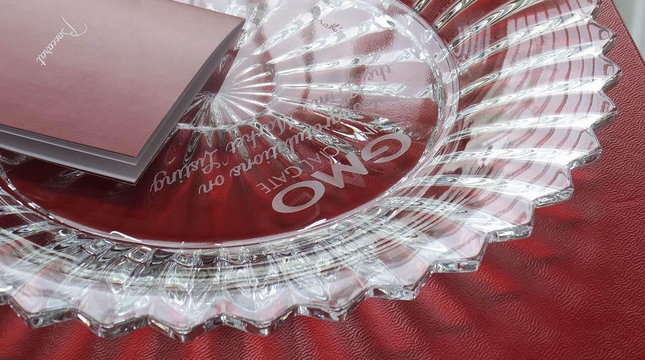 バカラの『ミルニュイ プレート』の中心部に、上場記念の豪華な特注彫刻を施したサンプル画像。プリーツ状の美しいカットが放射状に広がるクリスタル表面の上部に上場した企業のロゴ、中央に『祝・上場』や『Listing on Tokyo Stock Exchange』などの祝賀メッセージ、そして下部に贈り主側の企業ロゴが、極めて精細なエッチング技術で刻印されている。千の夜を意味するミルニュイの幻想的な輝きが、両社の強固なパートナーシップと、新たなステージへの飛躍を象徴する、最高峰のビジネスアニバーサリーギフトであることを表現している。