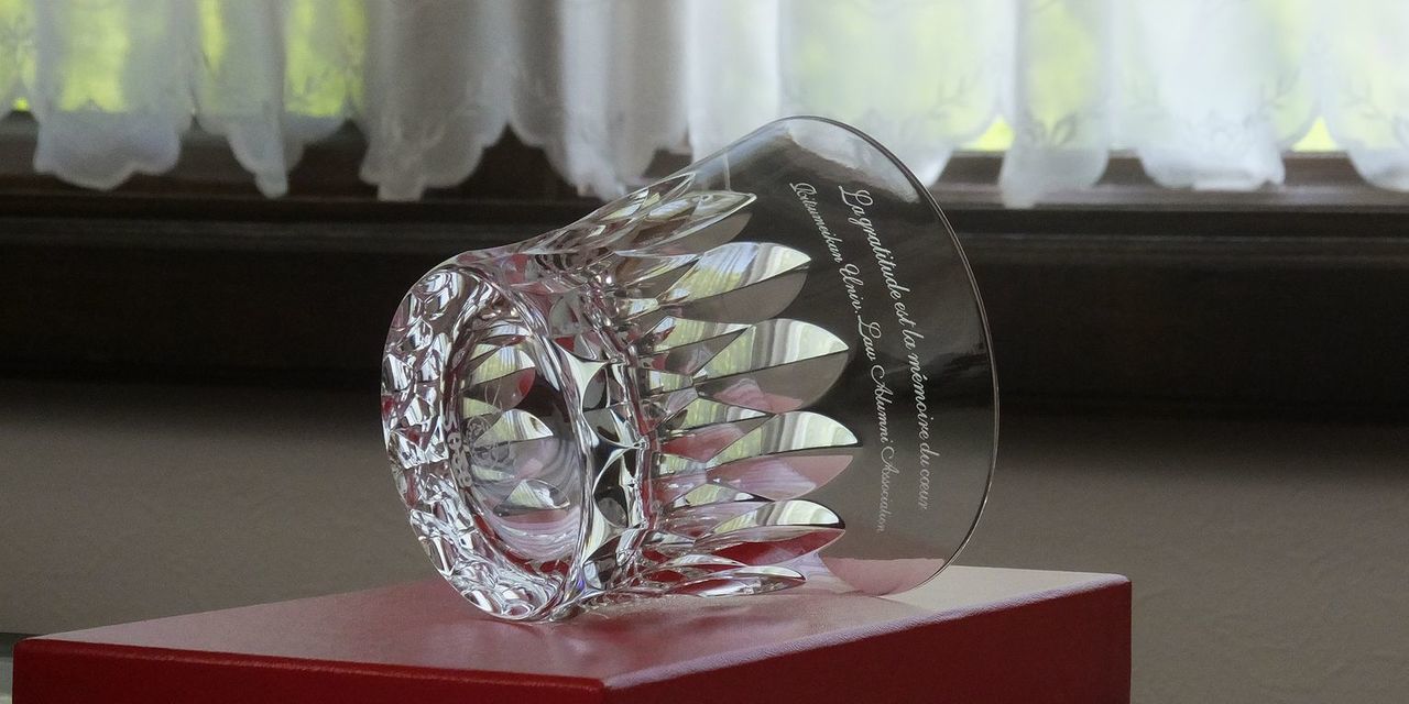 バカラ（Baccarat）の『ダリア』タンブラーの側面に、エレガントなフランス語のメッセージと『立命館大学法学部』の文字が精緻に名入れ彫刻された写真。大輪のダリアの花を思わせる華やかなカットワークと最高級クリスタルガラスの輝きが引き立ち、卒業記念、士業同士のお祝い、あるいは母校の功績を称える特別なギフトにふさわしい、洗練された品格あふれるイメージ。