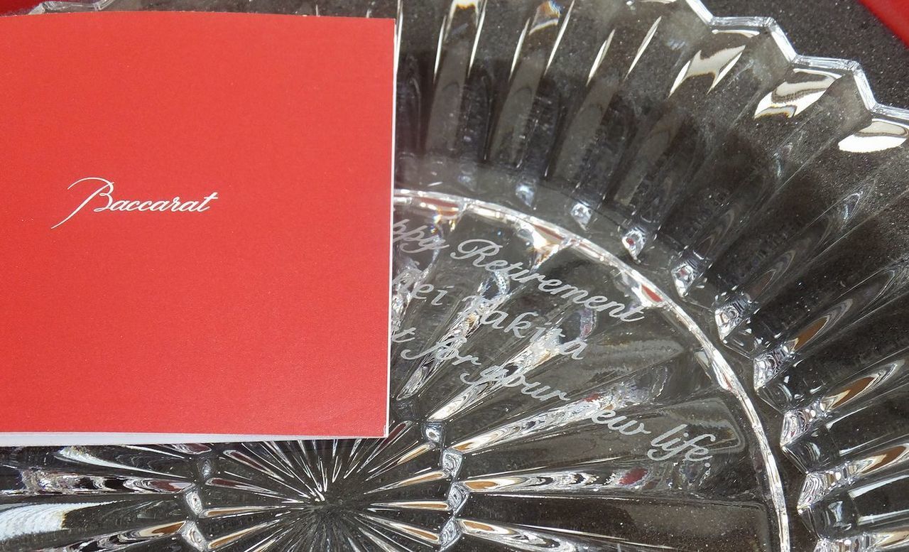 バカラの『ミルニュイ プレート』の表面に名入れ彫刻を施した退任祝い記念品の制作実績。「千の夜」を意味する名前の通り、プリーツのような美しい放射状のカットが特徴的なプレートの中央部に、企業ロゴマークとともに、『Happy retirement [名前] [メッセージ] [日付]』が精巧かつ上品に刻印されている。繊細なクリスタルの輝きと、組織を率いたリーダーへの敬意を込めたパーソナルなメッセージが調和し、長年の功績を称えるにふさわしい重厚で華やかな記念ギフトとして視覚的に表現されている。