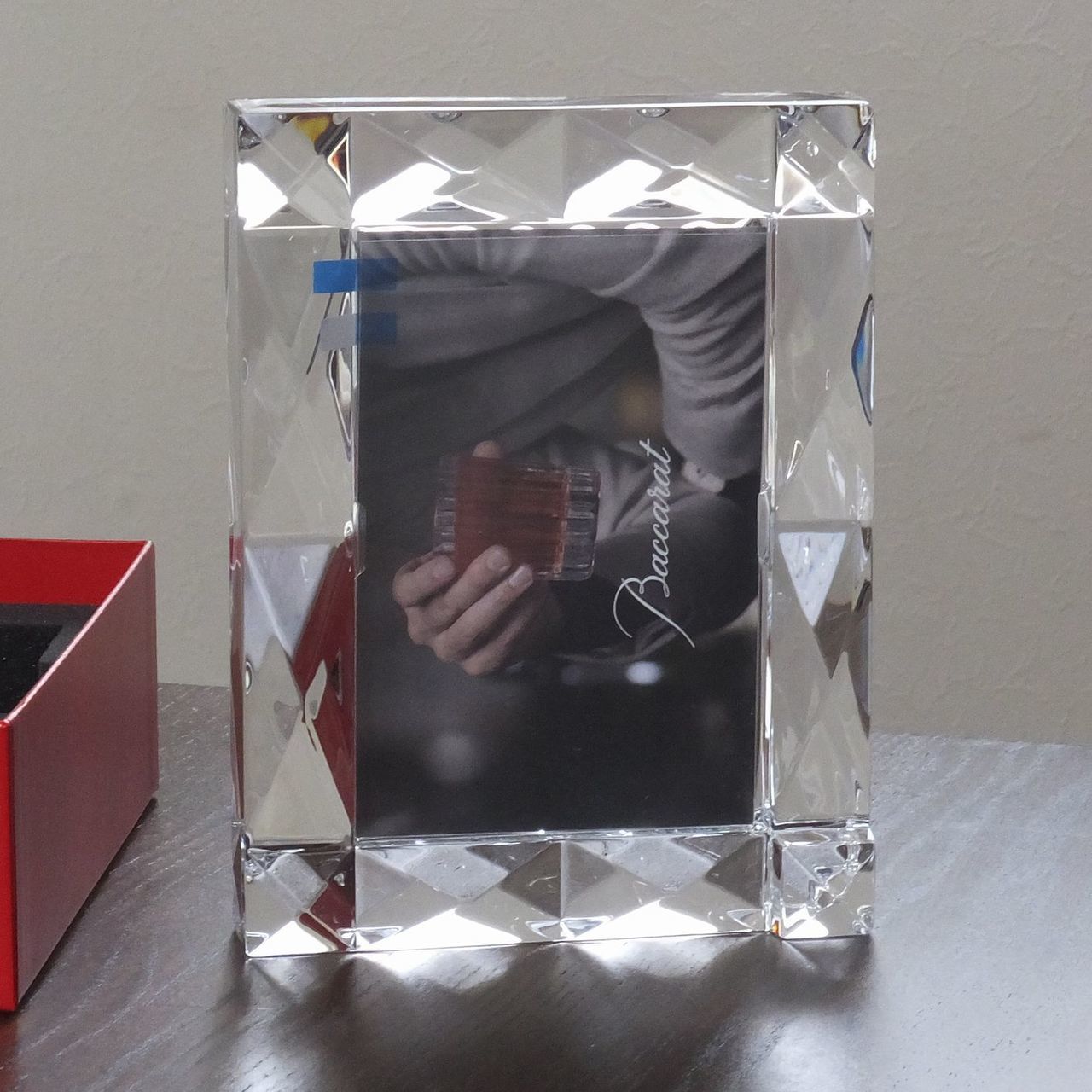 バカラの『ルクソール』フォトフレームを、テーブルの上に縦置き（ポートレート）で配置した写真。ピラミッド状のダイナミックなカッティングが光を垂直方向に反射し、クリスタル特有の輝きと重厚な透明感が際立つ。洗練されたデスクや棚の上で、大切な瞬間を芸術品のように引き立てる最高級インテリアのイメージ。