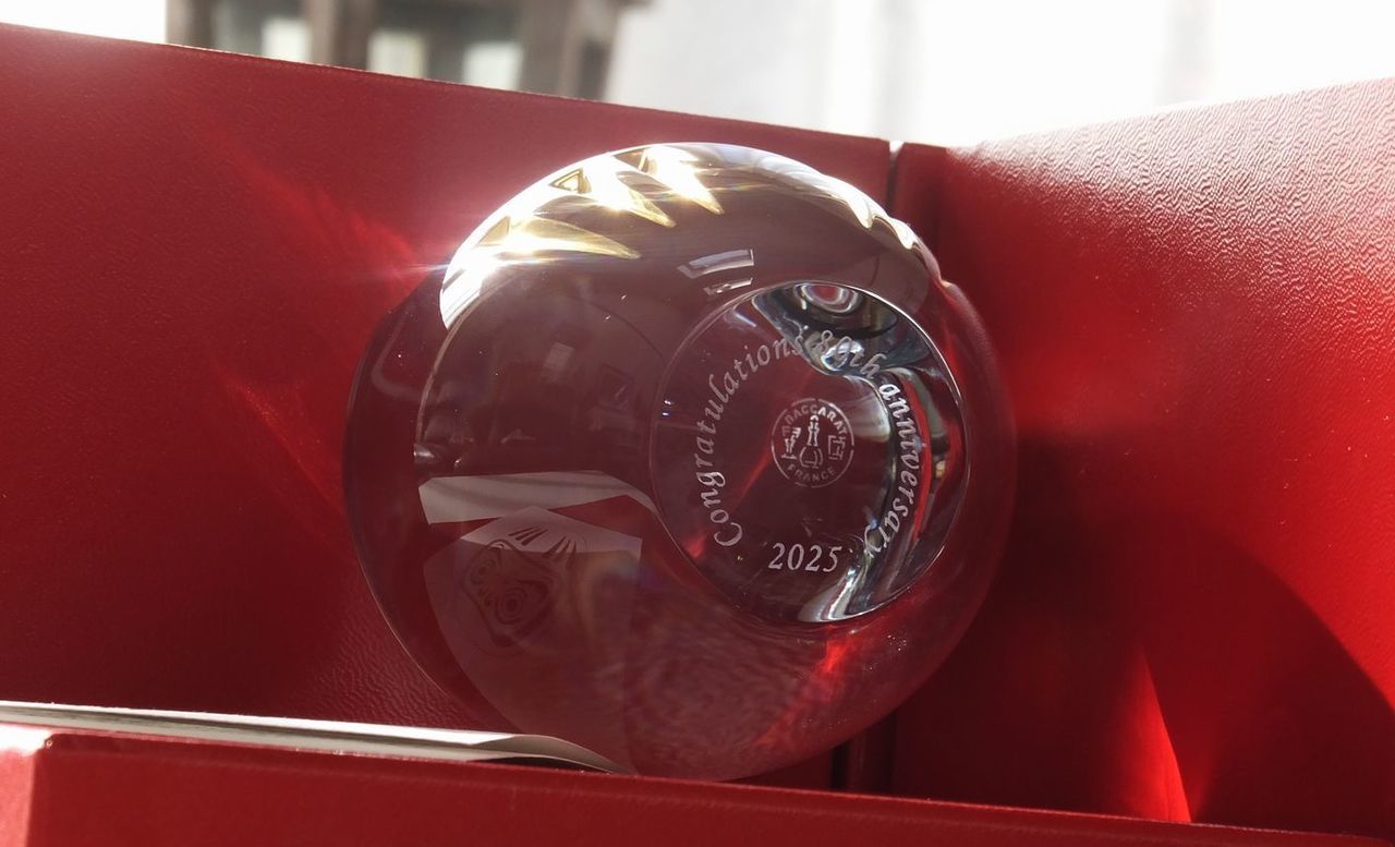 バカラのクリスタル製ダルマの底面に名入れ彫刻を施したサンプル画像。ダルマの安定した底面に、メッセージ『Congratulations 80th anniversary 2025』が英字セリフ体で精巧に刻印されている。幸運や願掛けの象徴であるダルマと、80周年という企業の重大な節目を祝うメッセージの組み合わせは、確固たる成功と未来への発展を願う格式高い記念品に最も適しており、重厚感と特別な意味を視覚的に表現している。