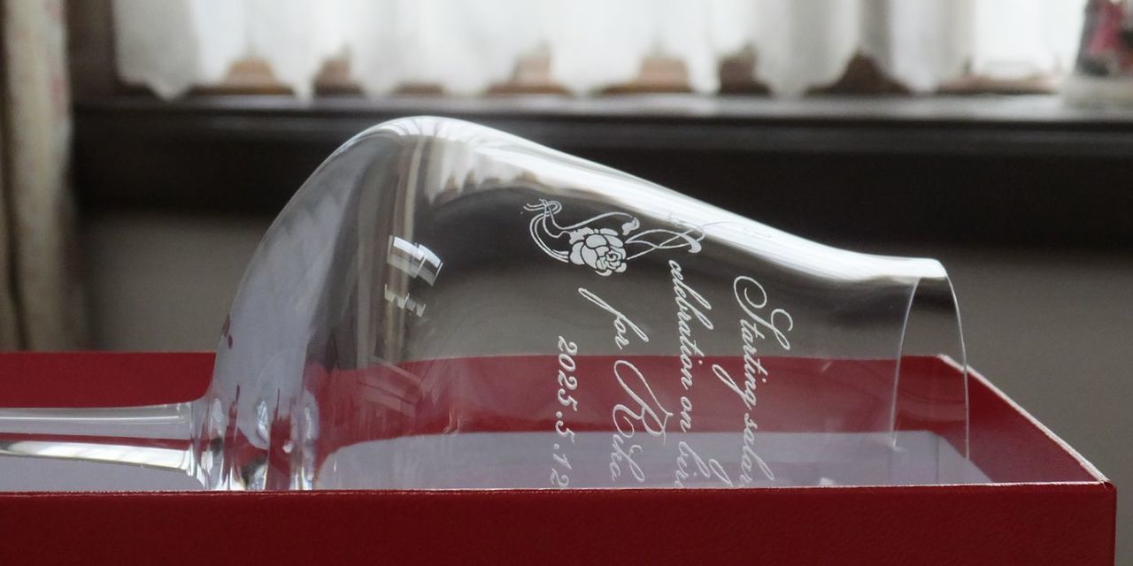 バカラ シャトーバカラ ワイングラス Lサイズのボウル(胴体)側面に、誕生日のお祝いメッセージ、日付、そして優雅なフラワーデザインを名入れ彫刻した写真。ブドウの房をモチーフとしたなめらかな曲線美を持つモダンなグラスに、華やかな祝福の言葉とデザインが融合し、人生を祝う特別なワイン体験を提供するアニバーサリーギフトとなっている。