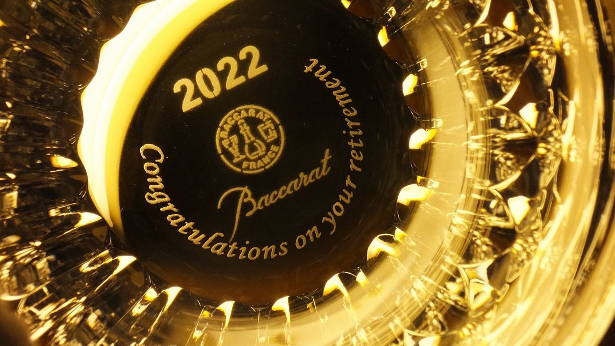 バカラの2022年限定モデル『クリスタ』タンブラーの底面に、格調高い英文フォントで『Congratulations on your retirement』とお名前、日付を名入れ彫刻したサンプル写真。水晶の石柱をイメージした力強いカットが光を反射し、底面に刻まれた退職への祝福と長年の功績への敬意をドラマチックに演出する、最高級の法人向け定年退職記念ギフトのイメージ。
