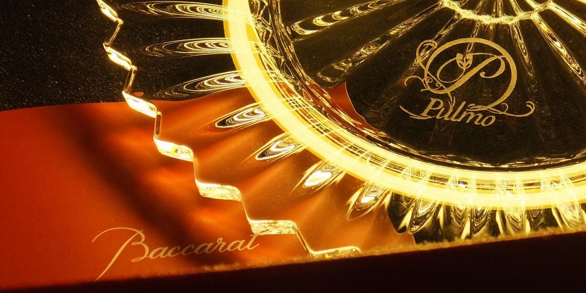 バカラ（Baccarat）の『ミルニュイ』プレートの上面に、医療法人のシンボルロゴデザインが精緻に名入れ彫刻された写真。『千の夜』を意味する放射状の美しく美しいプリーツカットが刻まれた最高級クリスタルガラスに、整ったロゴ刻印が印象的に映え、病院やクリニックの開院記念、創立周年祝い、あるいは役員就任などの祝賀にふさわしい、洗練された品格と信頼感を醸し出す記念品イメージ。
