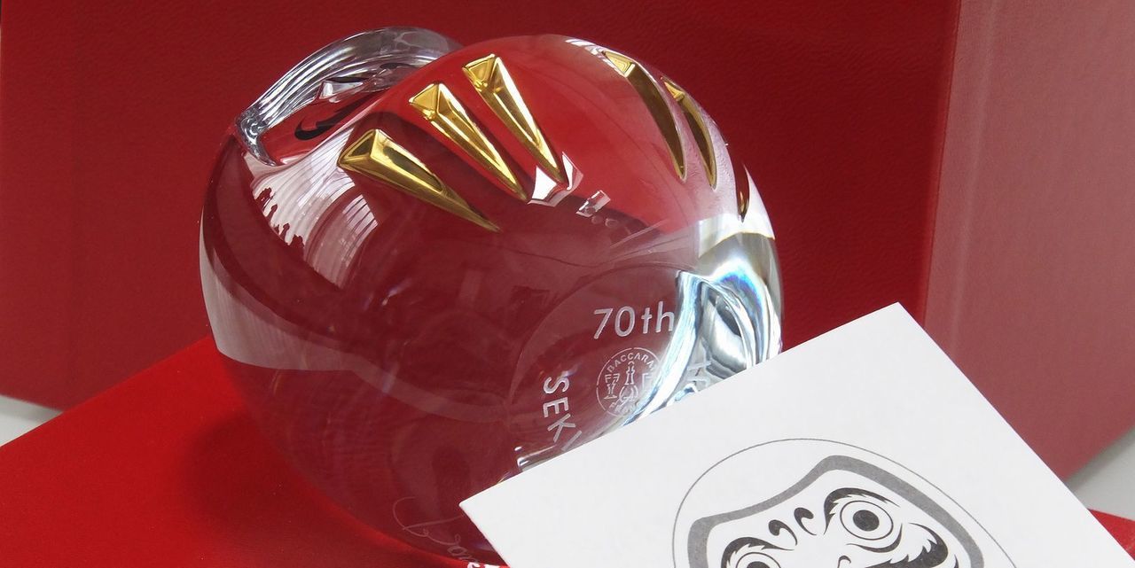 バカラのダルマの底面に『70th 株式会社〇〇』と名入れ彫刻を施した写真。透明なクリスタル製の愛らしいダルマの底に、企業の70周年を記念するメッセージと企業名が丁寧に刻まれています。企業の長年の歩みを称え、さらなる発展を祈念する、特別な周年記念ギフトにふさわしい逸品です。