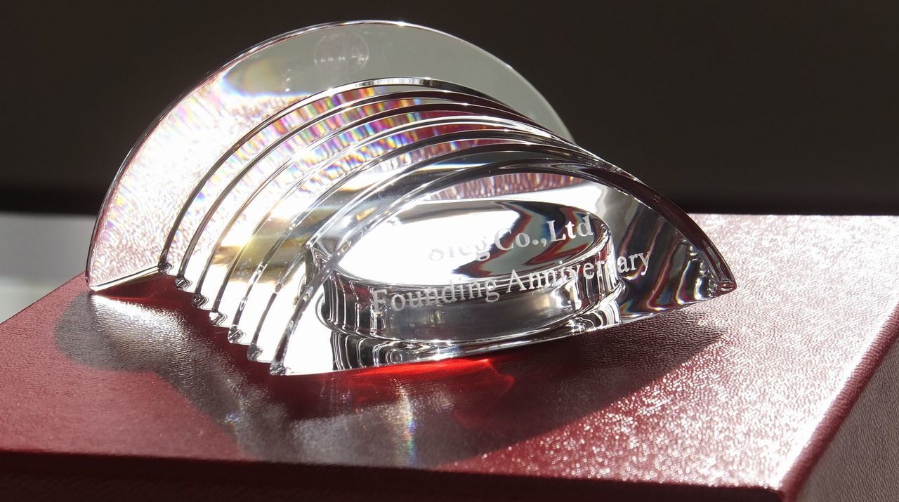 バカラのクリスタル製置き時計『ラランドクロック』に、企業の設立記念彫刻を施したサンプル画像。円形クリスタルの上部曲線に沿って、『Co., Ltd. Founding Anniversary』の文字が、洗練されたモダンな英字フォントで精巧に刻印されている。バカラ特有の完璧な透明度と光の屈折が、企業の原点となる設立の日を祝福し、これから共に刻んでいく輝かしい未来の時間を象徴する、品格と信頼に満ちたアニバーサリーギフトであることを視覚的に表現している。