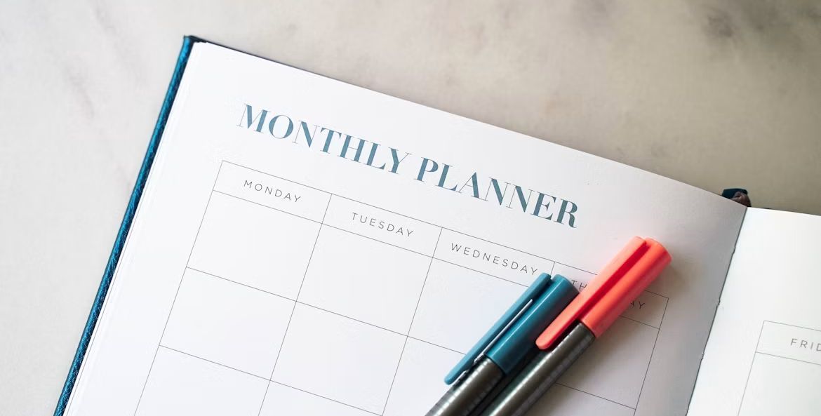 「Monthly planner」と書かれたスケジュール帳と青赤のペン