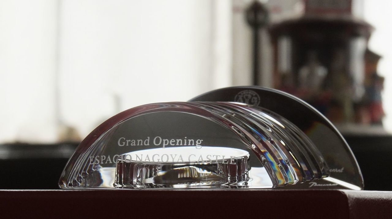 バカラのクリスタル製置き時計『ラランドクロック』に、ホテルの開業記念彫刻を施したサンプル画像。天文学者の名を冠した星のような円形クリスタルの上部に、『Grand Opening ESPACIO NAGOYA CASTLE』の文字が、高級感溢れるエレガントな英字フォントで精巧に刻印されている。バカラ特有の清澄な輝きが、名古屋の新たなランドマークとなるラグジュアリーホテルの誕生を祝うにふさわしい至高の品格を放ち、輝かしい門出と永遠に続く時を象徴する特別なギフトであることを視覚的に表現している。