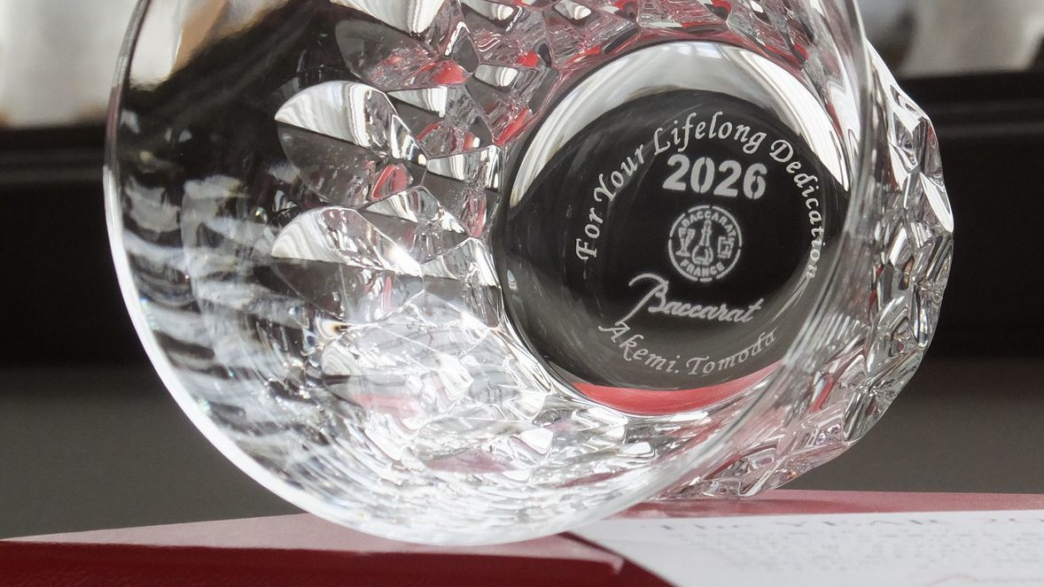 バカラの2026年限定モデル『ダリア』タンブラーの底面に、格調高い英文フォントで『For your lifelong dedication（長年の献身に感謝を込めて）』とお名前、日付を名入れ彫刻したサンプル写真。2026年の年号が刻まれたクリスタルの底面に、長年の功績を讃えるメッセージが光を反射して浮かび上がる、最高級の法人向け退職記念・永年勤続表彰ギフトのイメージ。