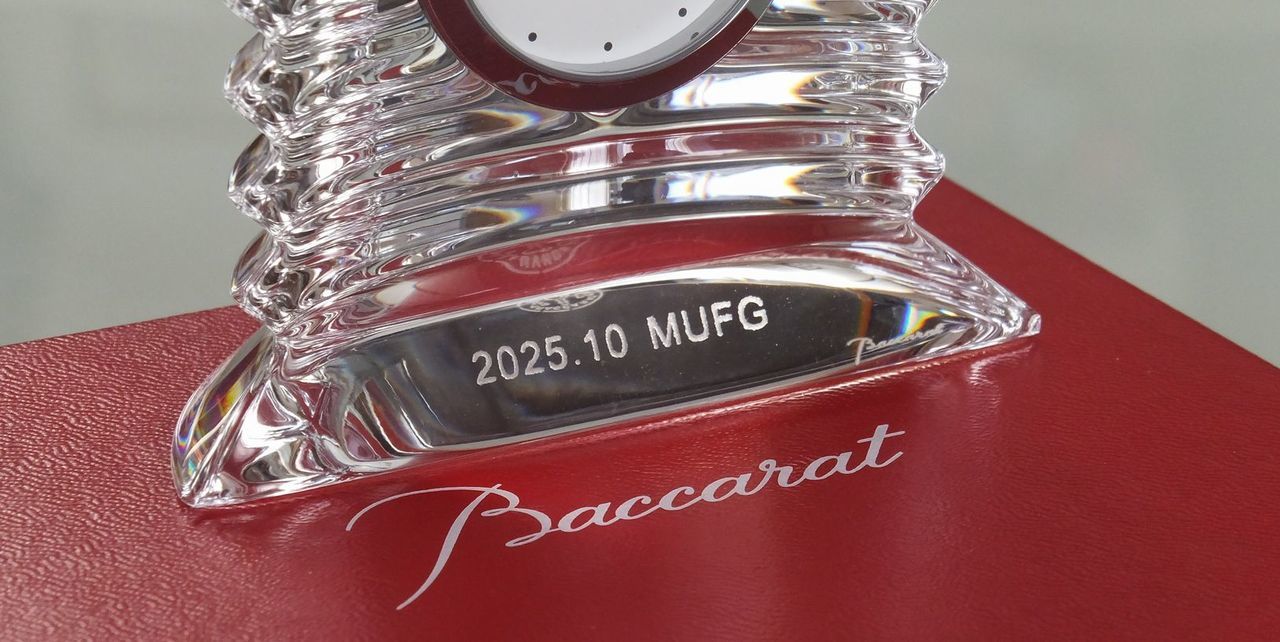 バカラ（Baccarat）のクリスタル製置時計『ラランド クロック』の前面台座部分に、『2025.10 MUFG』の文字が精緻に名入れ彫刻された写真。最高級クリスタルガラスならではの透き通るような輝きとカットワークに、格式高い刻印が鮮明に映え、メガバンクをはじめとする大手金融機関の創立周年記念、取引記念、あるいはVIP顧客への特別なお祝いにふさわしい、重厚感と信頼感を備えた格調高いイメージ。